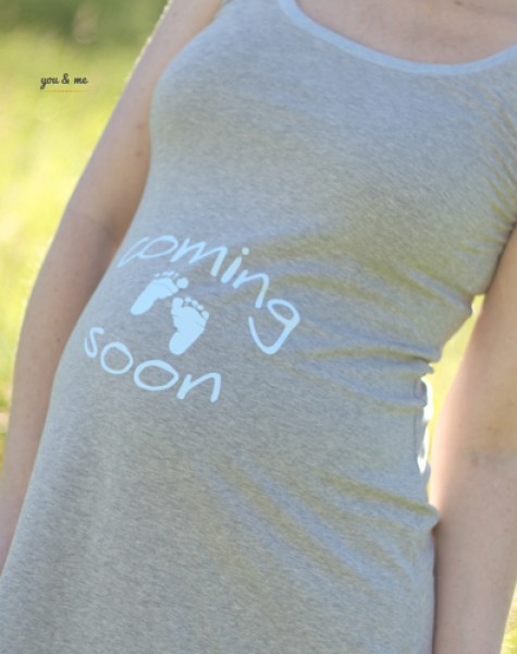 schwangere blonde Frau im Kleid mit Aufdruck Coming soon und Babyfüsse
